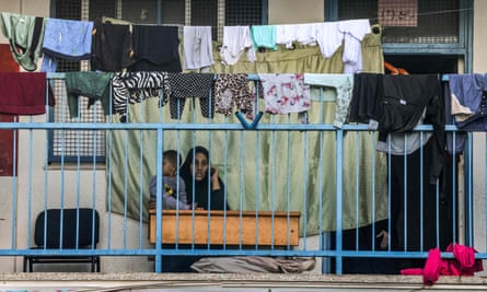 A woman speaks on a phone while carrying a child by drying laundry outside a classroom 