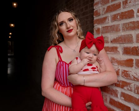 Aubrie Morris in red and pink holding baby with bow on head.