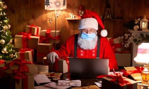 Santa wearing face mask holding Christmas gift on xmas eve using laptop