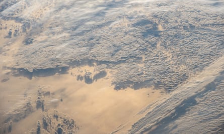 A photo taken from the International Space Station shows the sun reflected off snow and ice with clouds and shadows making a surreal landscape.