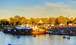marquees and people on the banks of a river in part shade, part sun