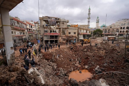 People inspect a crater amid the damage of an airstrike