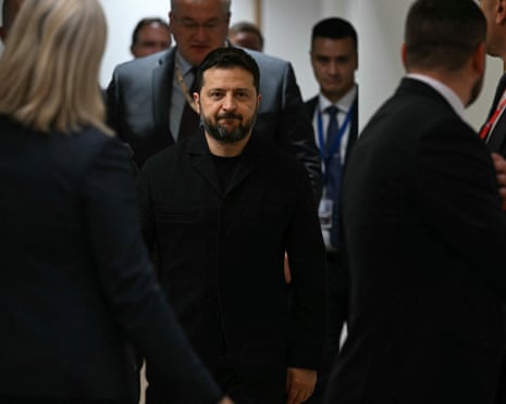 Volodymyr Zelenskyy walks through a corridor surrounded by people in suits.