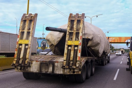 the barrel of a tank’s gun pokes out from under tarpaulin on a vehicle transporting it