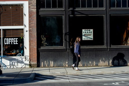 A woman walks on a city street in front of a coffee shop and empty store front