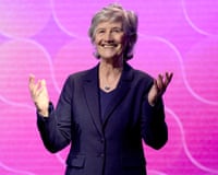 Head and shoulders picture of Catherine Connolly, wearing a dark suit and smiling, with her hands raised, against a pink background