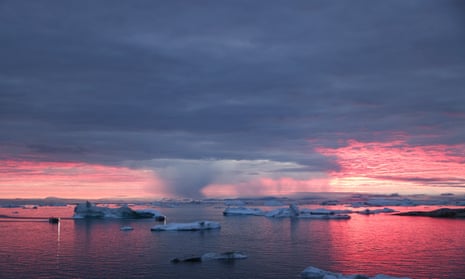 The sun sets as rain falls beyond floating ice and icebergs in Disko Bay, Greenland