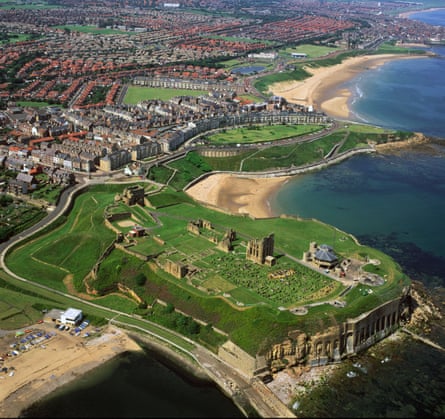 Aerial view of a grassy headland with ruin on top and sandy beaches either side