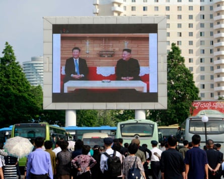 people watch a big screen showing Xi Jinping and Kim Jong-un smiling at their last meeting in 2019