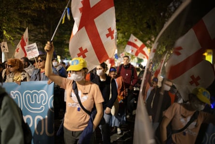 a crowd in a dark street holds red and white Georgian flags