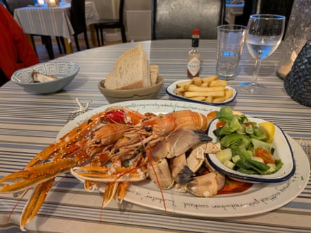 A table laid with a plate of seafood, a side salad, a bowl of chips and a bowl of bread and butter.
