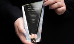 A woman's hands with lavender fingernails hold a glass trophy with the words "NYU Langone Health" and an indication the award was for 'compassionate care.'