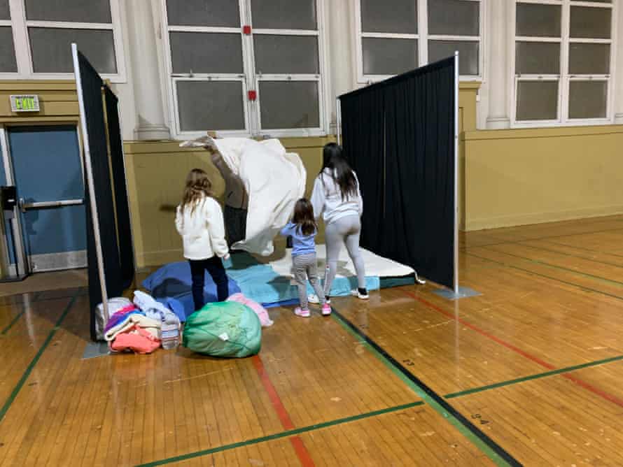 A mother and her three daughters make up a bed in a partitioned cubicle in a school gymnasium.