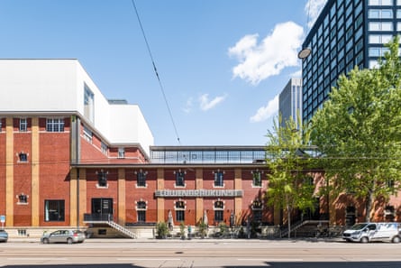 A red-brick building, with trees in front and a tower block to the side.