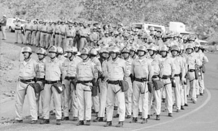 A black and white picture of quads of Arizona Department of Public Safety officers stand across the road from the entrance to the Phelps Dodge mine at Morenci, August 1983.
