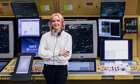 Air traffic controller Kim Gough, standing, with headphones around her neck, and multiple screen and control buttons behind her