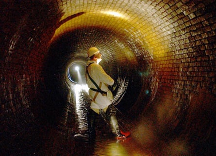 Worker in hard hat standing in a wide, round sewer tunnel