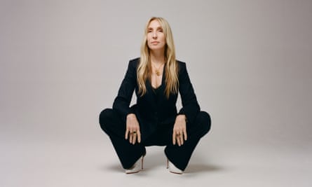 Sam taylor-Johnson, in a dark suit, crouches for a portrait, looking at the camera