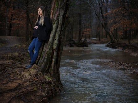 A pregnant woman leaning on a tree above a creek.