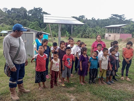 18 children stand in front of solar panels in a clearing