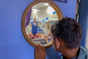 A person looking through a circular window in a door. On the other side are medics examining two young girls covered in blood