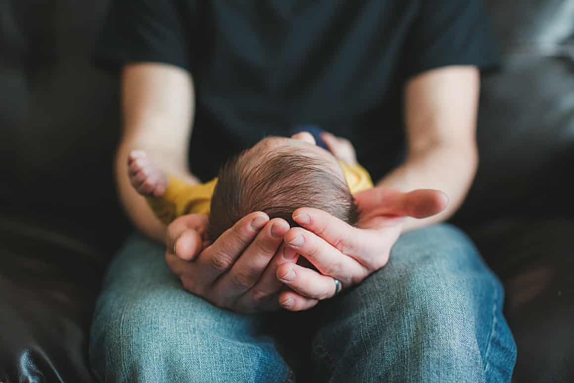 Fathers hands holding newbornNewborn baby boy with dark brown hair lays cradled in his fathers hands.
