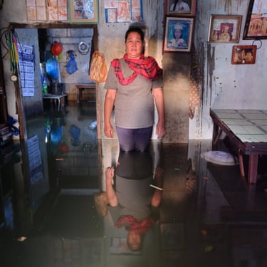 A woman stands knee-deep in flood water inside his house