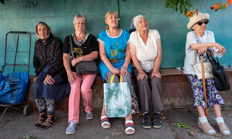 Five older Ukrainian women sit in the shade while the wait for food distribution to begin in the city of Mykolaiv.