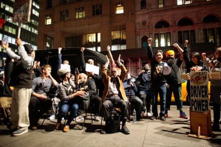 A crowd of people stand outside raising their fists next to a sign that says ‘driver power’