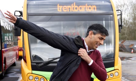Sunak putting his jacket on in front of a bus
