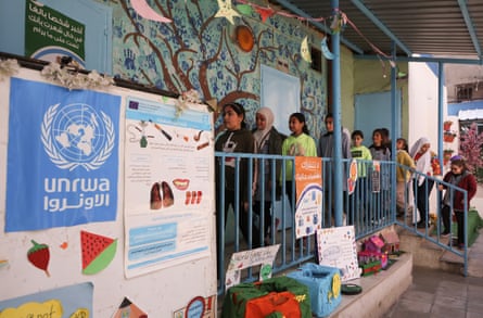 Young girls with their faces painted file into a classroom decorated with a mural of a tree and handprints