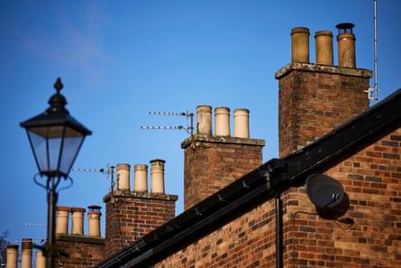 View across the roofs and chimneys of a row of brick terraced houses against a blue sky.