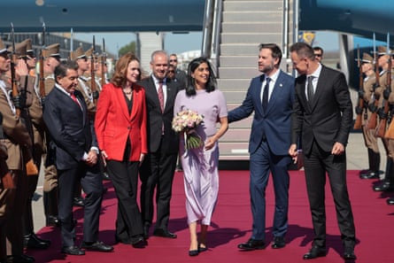 Péter Szijjártó greets JD Vance and Usha Vance as they step off Air Force Two on to a red carpet at the airport in Budapest. An armed guard is stood on either side of the carpet