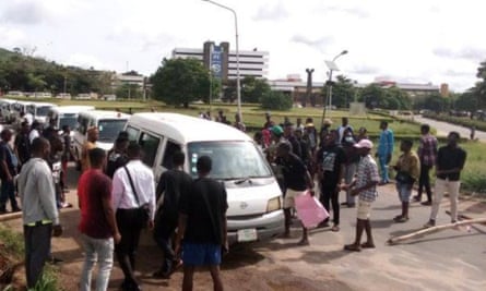Students protest around a parade of white vans.
