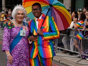 A drag queen dressed as Queen Elizabeth II next to a man in a rainbow suit holding a rainbow umbrella
