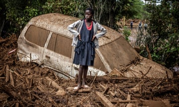 A girl stands next to a car partially buried in mud