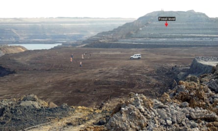 A large mine with six people and a large car on a flat area at the surface. A red arrow points to the level at which the fossils were found highlighted.