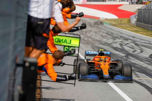 Lando Norris passes his team as they celebrate on the pit wall