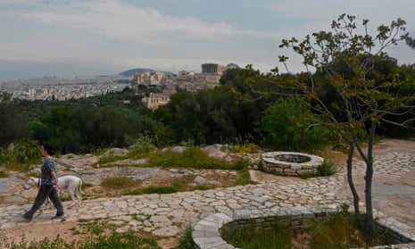 A woman walks her dog at an empty touristic spot in Athens overlooking the Ancient Acropolis and Athens city on 21 April.