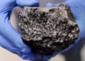 A black otherworldly rock held by hands in blue rubber gloves.