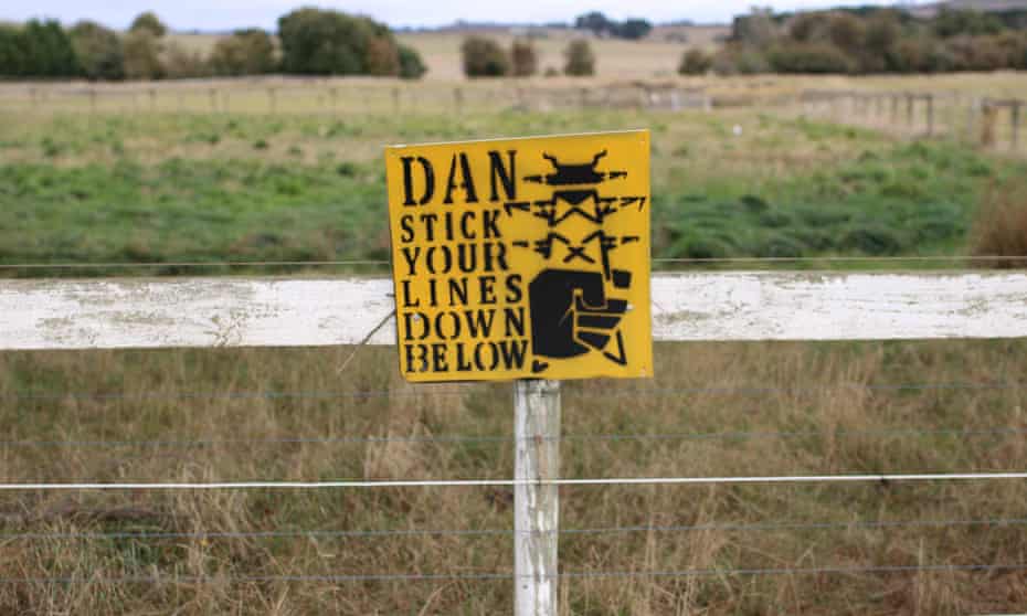 A homemade sign saying &quot;Dan stick your lines down below&quot; next to an image of a tower is stuck to a white fence in farmland in Blampied, Victoria