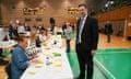 A man in a suit watches over a table of people counting ballot papers