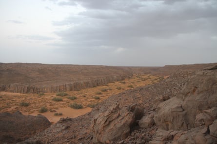 A shot from high up showing a rocky red and brown landscape with sparse, scrubby vegetation