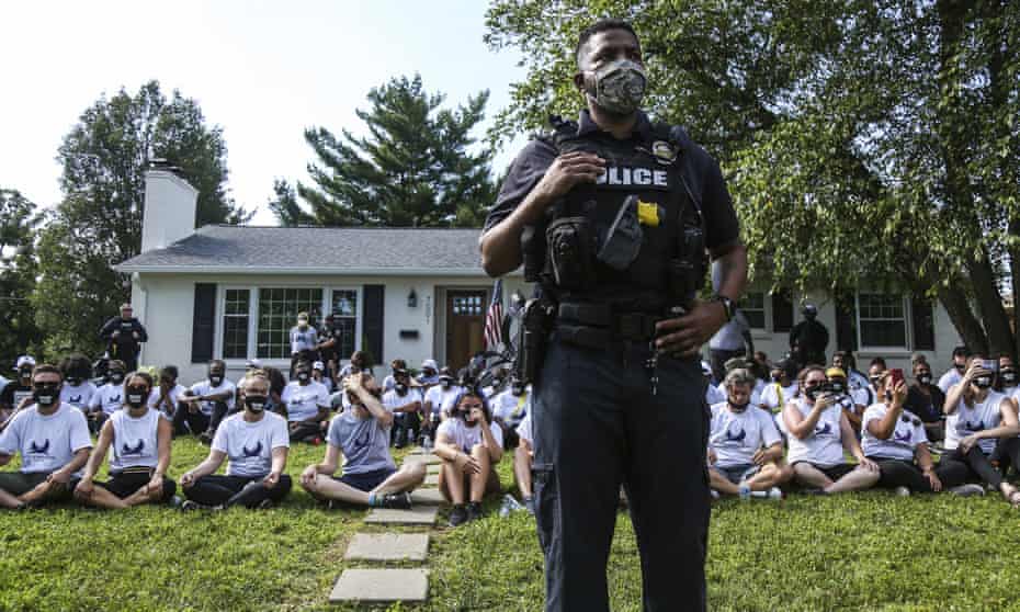 In this image from video, a Louisville Metro Police Department office stands guard outside the home of Kentucky Attorney General Daniel Cameron as protestors sit in his front yard in Louisville, Kentucky Tuesday, July 14, 2020. About two dozen protestors were arrested. Protesters were chanting Breonna Taylor’s name as well as calling for justice after the 26-year-old emergency room technician was fatally shot by LMPD in her South End Apartment while police were serving a search warrant. Cameron said he still has no timeline for when his office will conclude its investigation of the case. (Mary Ann Gerth/Courier Journal via AP)