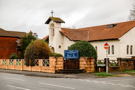 A small white church with a bell tower and orange tiled roof behind a low wall and sign
