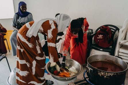 Three young Senegalese women in a dahira in Gran Canaria, Spain, prepare food in large metal pots.