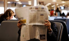 Person sitting and holding a newspaper, covering their face.