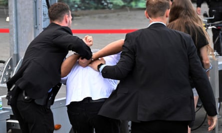 A man with his hands cuffed behind him is led away by two bodyguards
