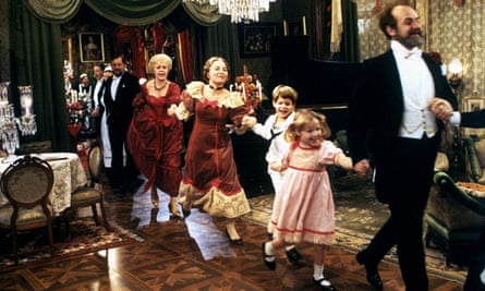 Men, women and children in period dress dance in a line in an old fashioned living room