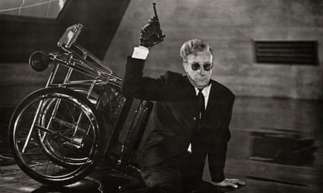 black and white film still of man sitting on the floor next to a wheelchair wearing a suit and sunglasses with a gun in the air